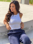 A woman sitting outdoors on a concrete ledge wearing a Be Athletica Be 180 Racer Tank in White and Varsity Athletica Midnight Sweatpants in Midnight.