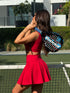 A woman on a padel court wearing a bright red Be Athletica Be 180 Sports Bra and Be 180 Skort in Cherry.